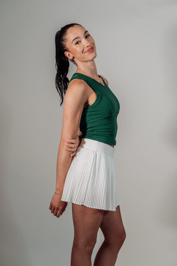 Side view of model Nikki wearing the white pleated Good Dink skort and green Good Dink woman's tank top