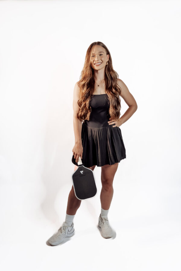 Front view of model Kae wearing black pleated Good Dink pickleball dress